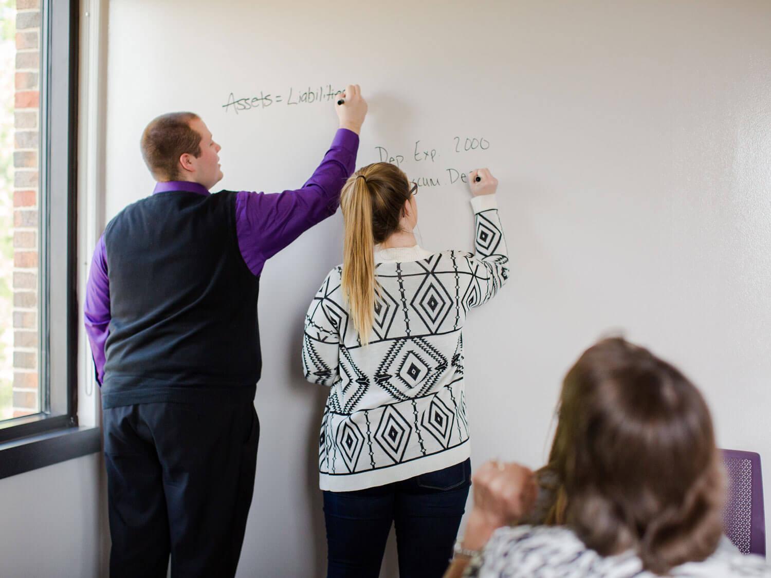 Students work out accounting problems on whiteboard