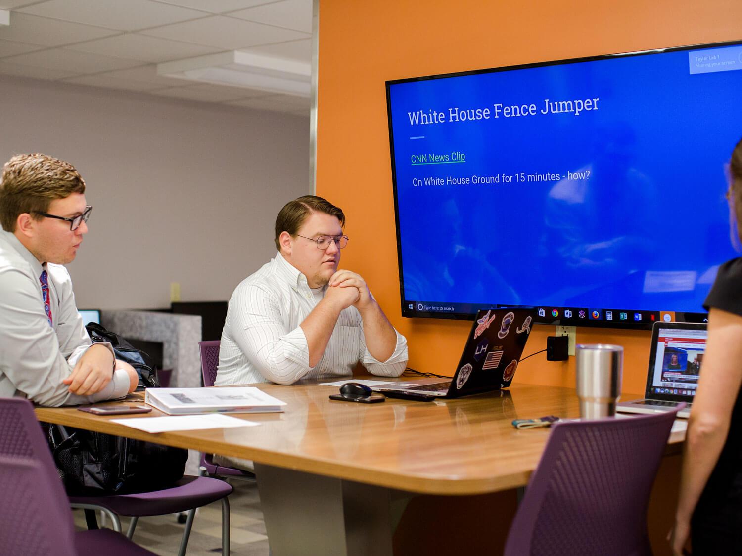 Students practice a group presentation in front of large computer monitor