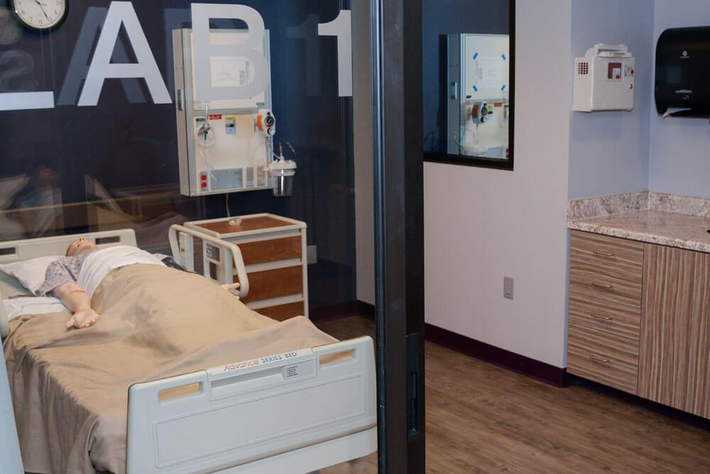 Looking through window at mannequin in hospital bed in simulation lab