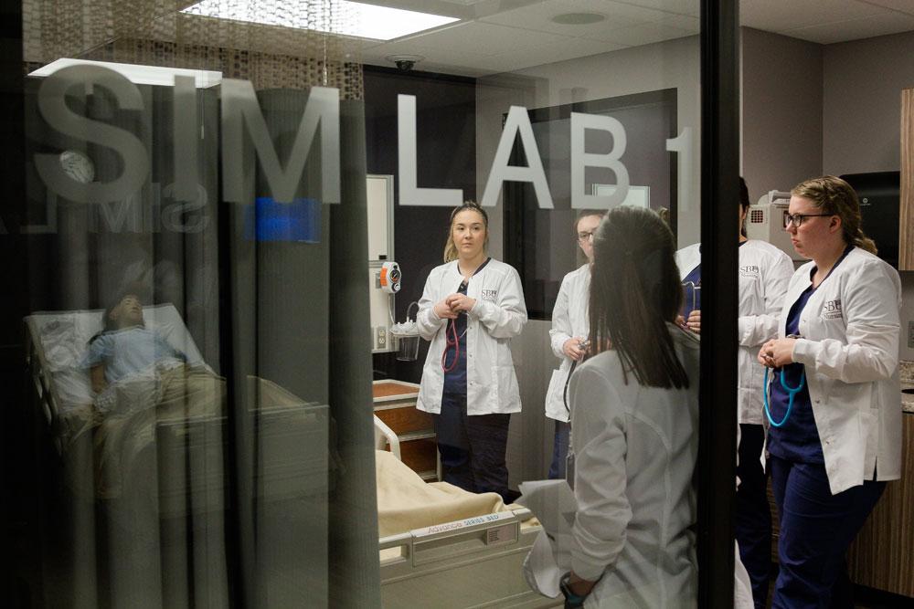 Group of nursing students listen to instructor inside a simulation lab