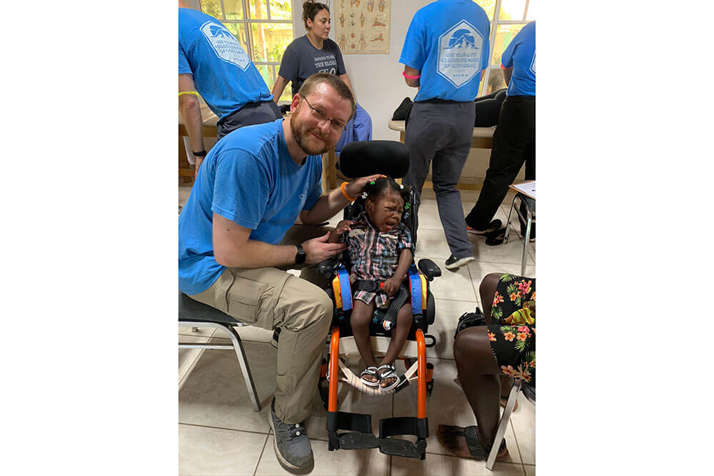 SBU Physical Therapy professor smiles while sitting next to small Haitian girl in wheelchair