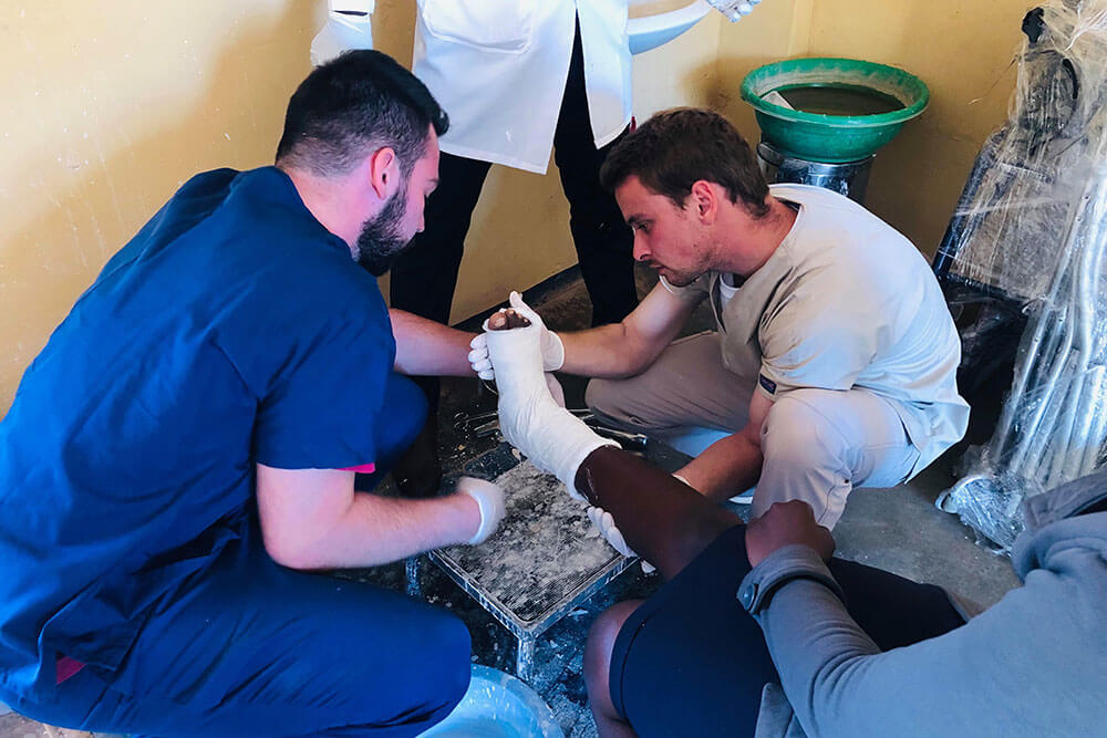 Two male physical therapy students examine cast on patient's foot