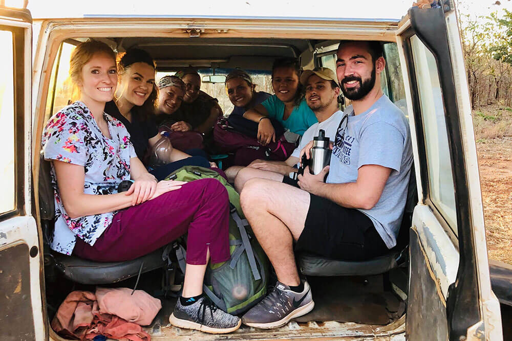Eight physical therapy students crammed into back of a jeep on a dirt road