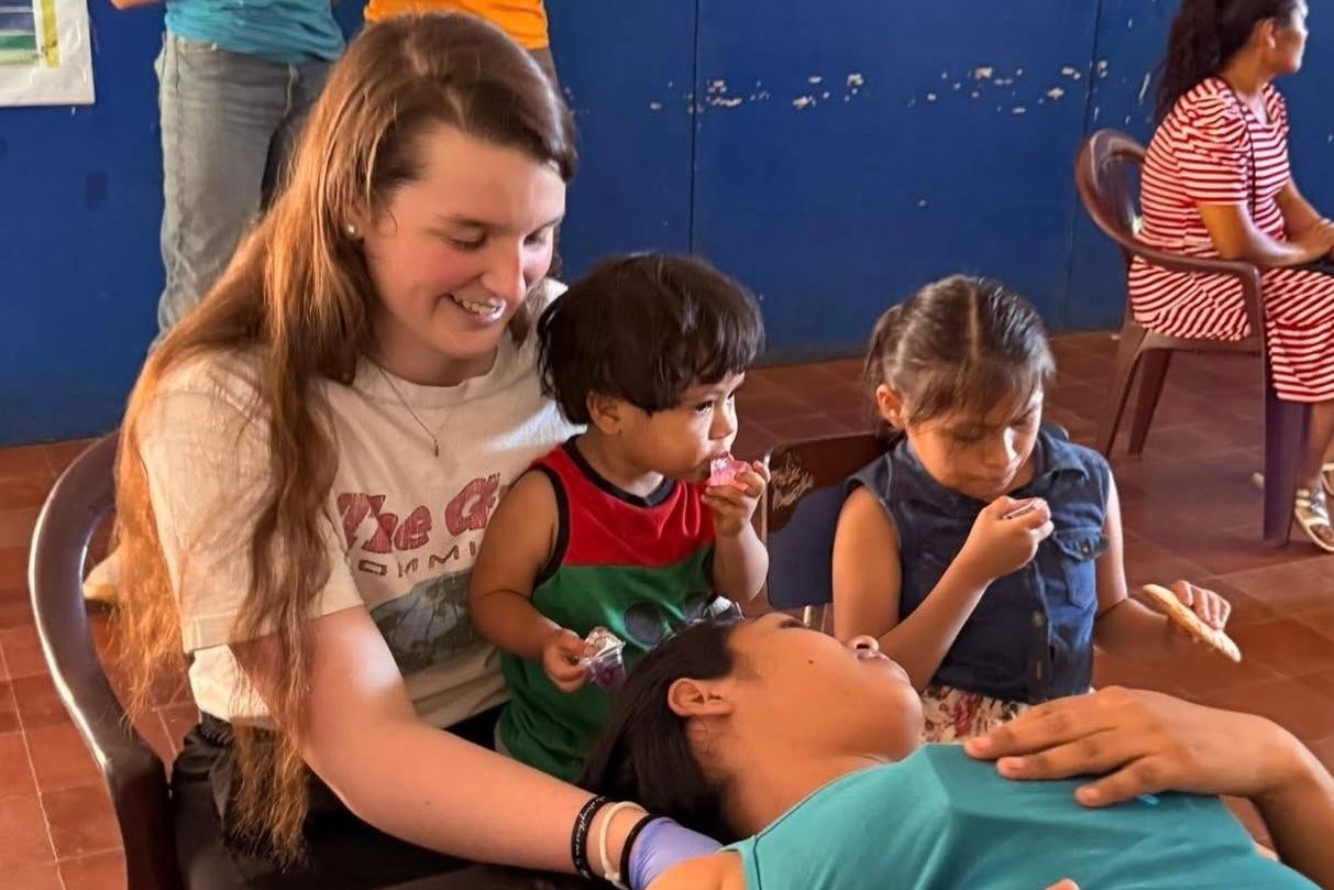 Physical therapy student performs exam while holding a young child in El Salvador 
