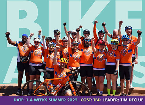 large group of cyclists in orange cycling group pose with fist pumped in air