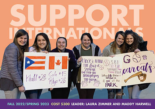 six girls smile and hold poster board signs handmade to support student-athletes; text in background says support internationals