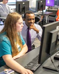 Dr. Gichamba sitting next to student looking at computer screen 