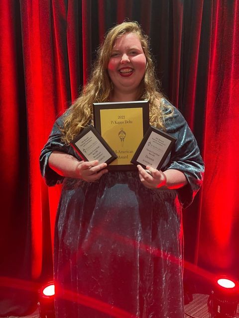 Jessica Paxton stands in front of red stage curtain holding award plaques