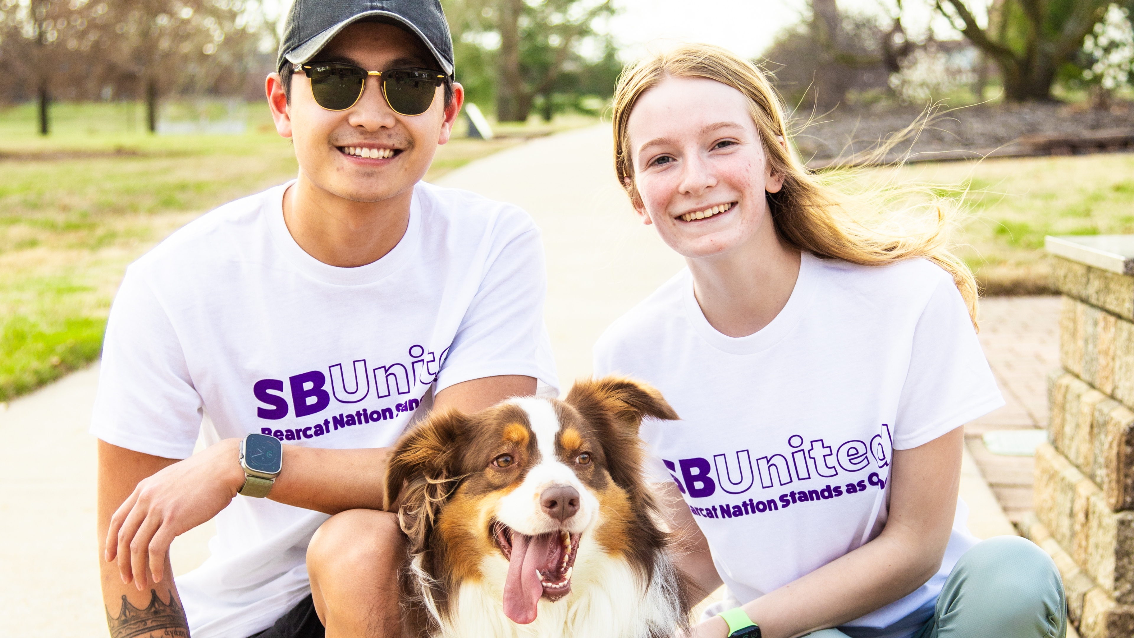 Two students smiling with dog wearing SBUnited shirts