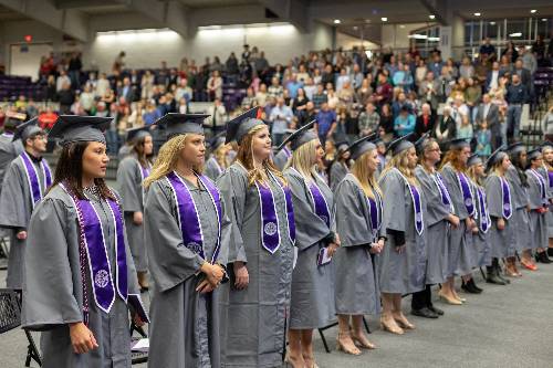 associate degree graduates stand in front of stage