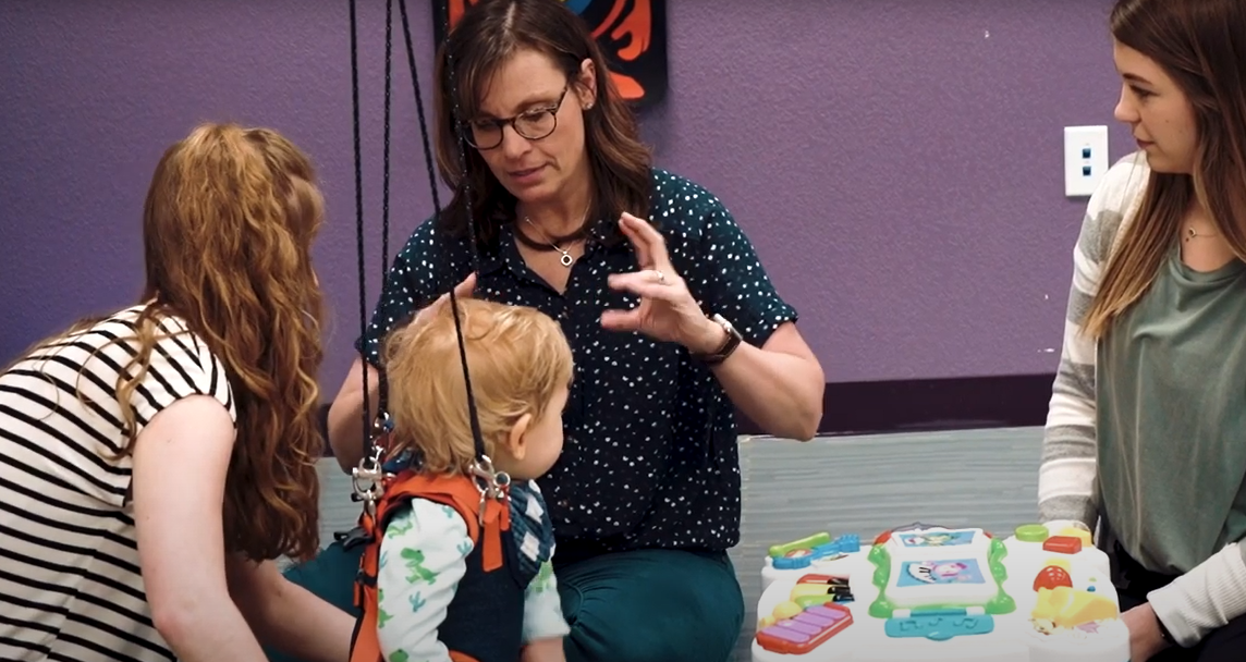 physical therapy professor instructs students while working with toddler patient