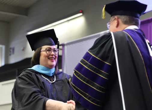 female master's of education graduate smiles as she receives diploma from university president