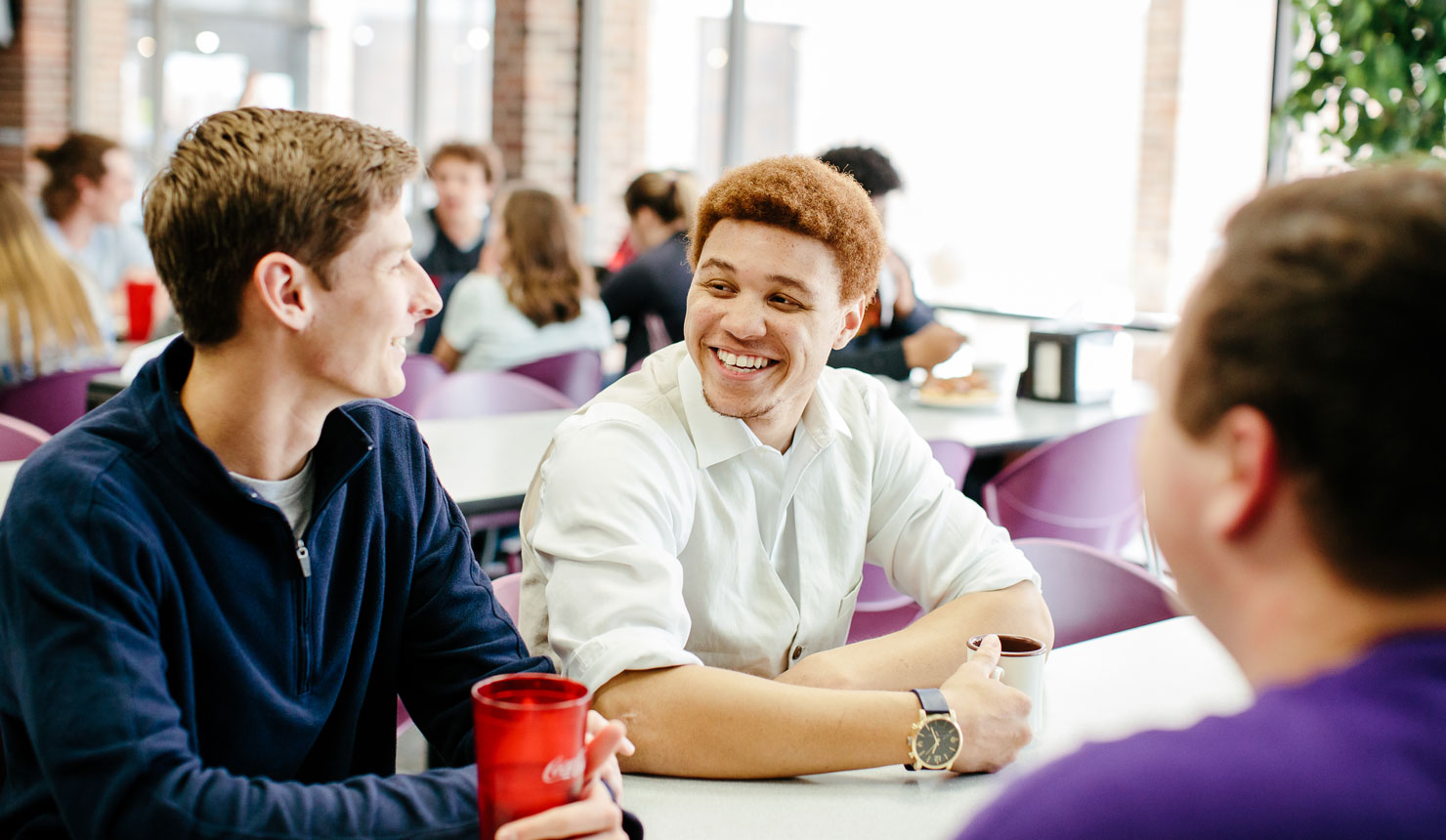 two guys smile while talking to each other sitting at cafeteria table