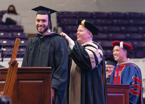 male graduate receives hood from professor during commencement ceremony