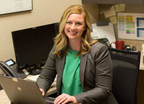 female business professional smiles while sitting at desk in front of computer