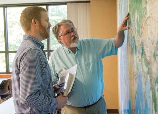 professor points to large map on wall while talking to student