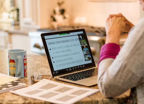 view from behind as teacher sits with laptop at kitchen table