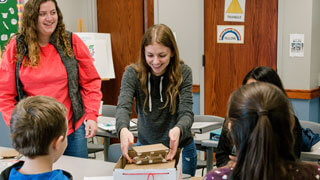 female college students smile while working on project with kids