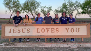 group of college students standing behind sign that says Jesus Loves you