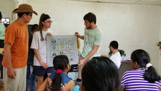 three college students at front of classroom of middle school students in Panama holding chart and doing demonstration
