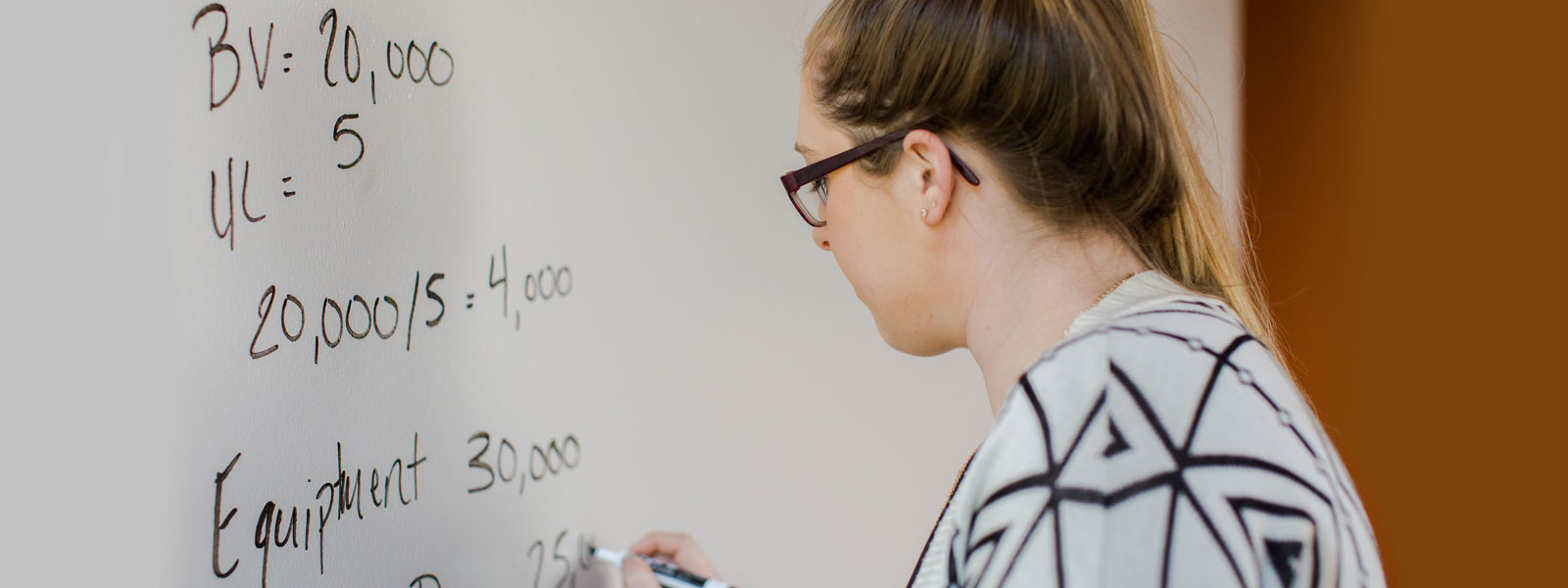 student works on accounting problem on whiteboard