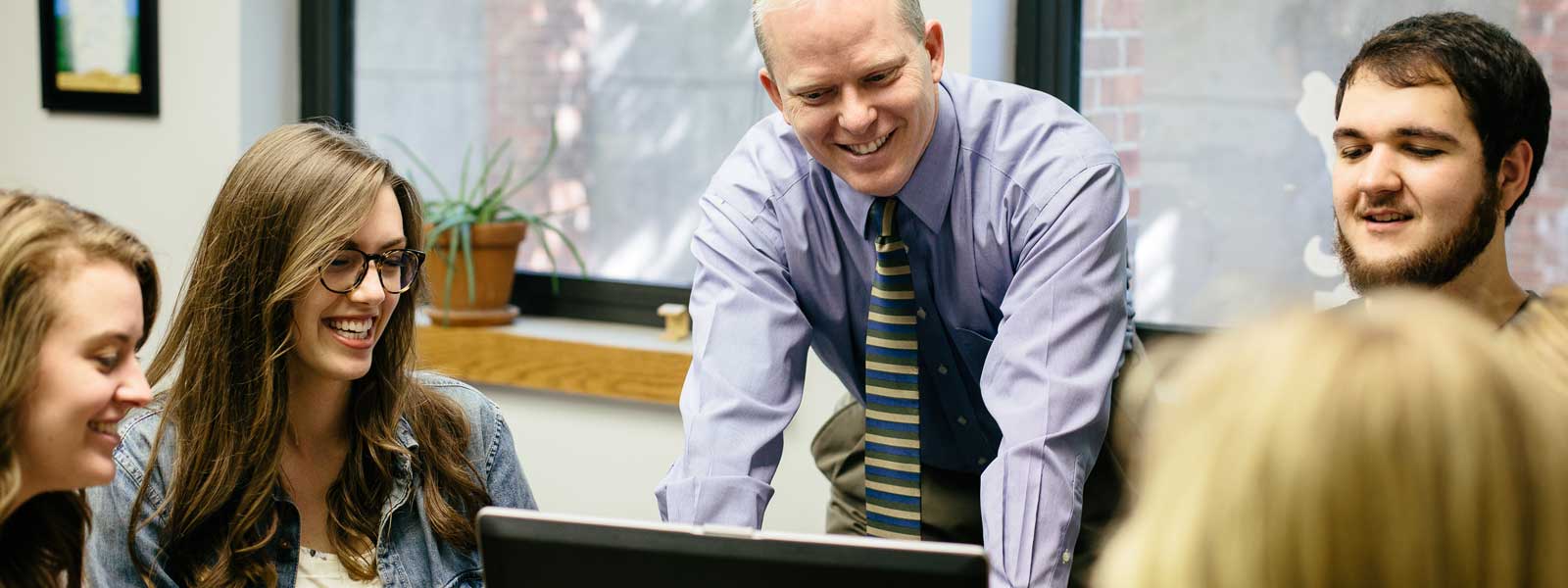professor laughs with group of students working on project