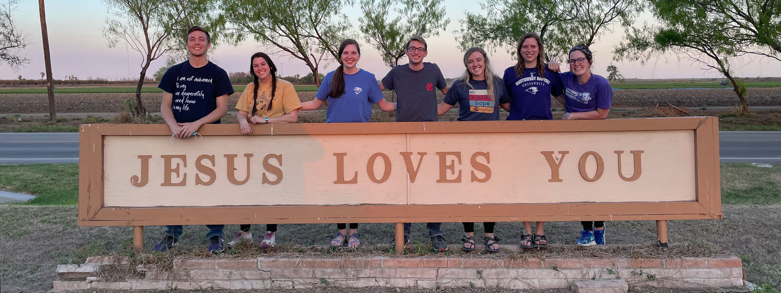group of college students standing behind sign that says Jesus Loves you