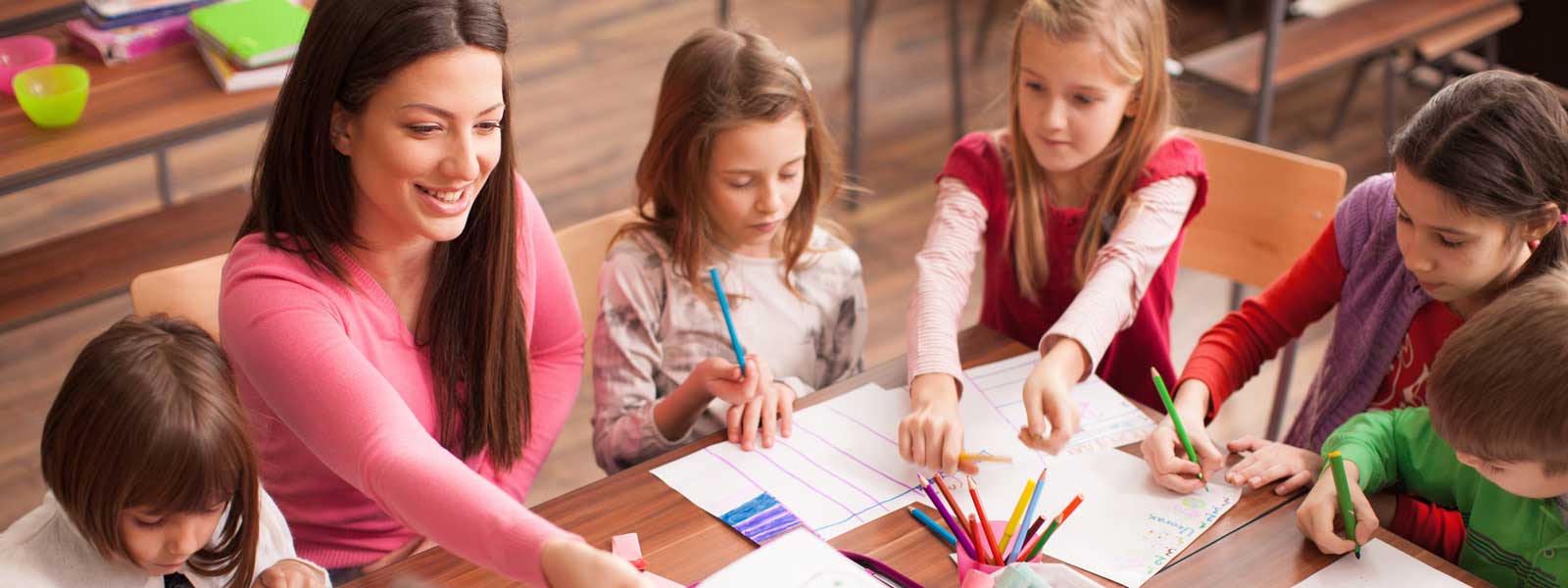 teacher works with students at table in elementary classroom