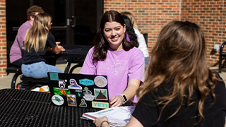 marketing professor leans over table to help group of students