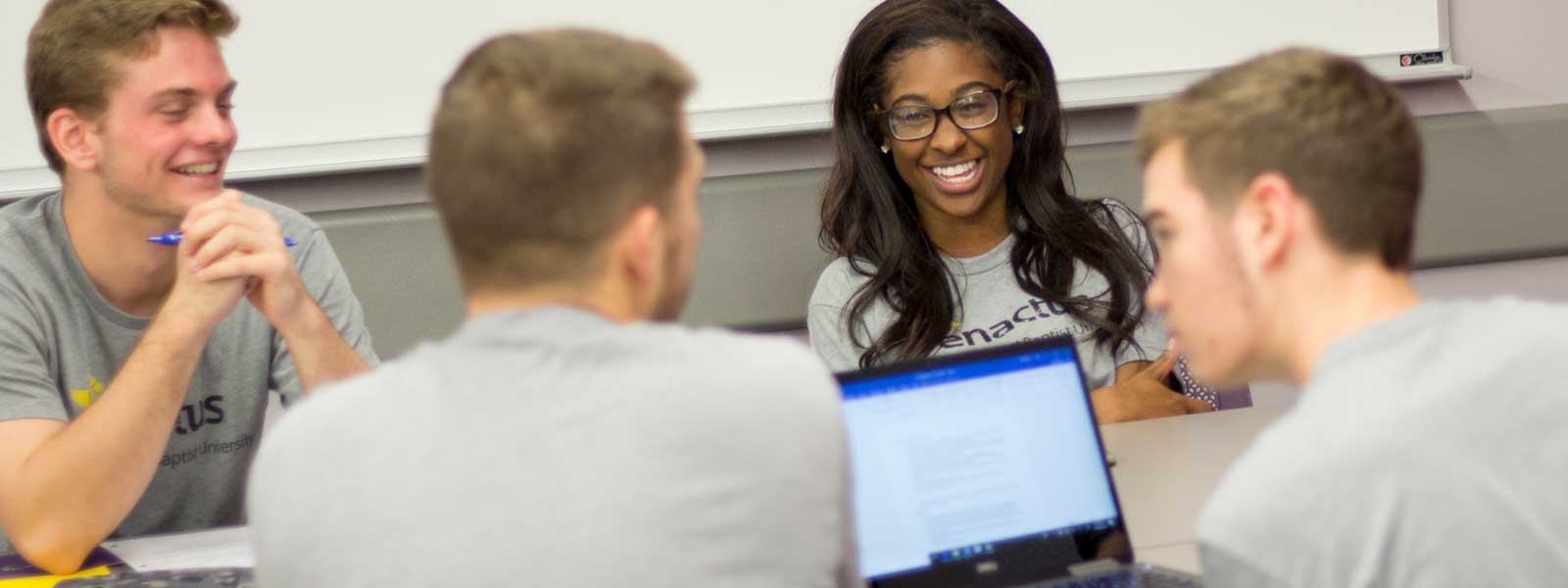 group of students laughing while working on school project using laptop