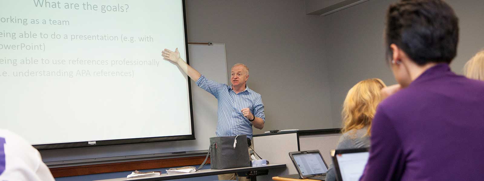 sociology professor gives class lecture while students take notes on laptops