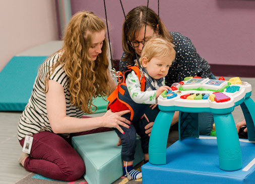 physical therapy student and professor work with toddler learning to walk