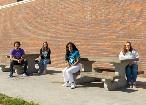 Four student leaders sit at concrete picnic tables outside