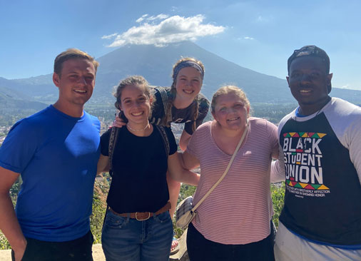 five students smile for picture with volcano in background