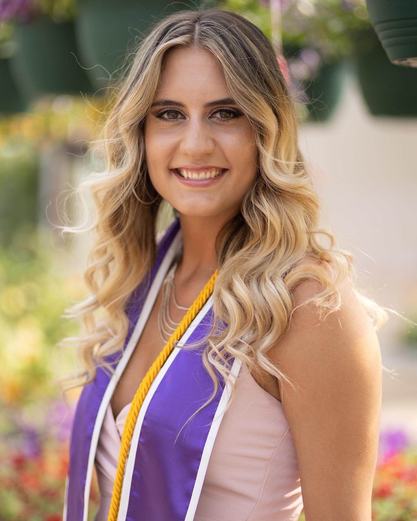 Haleigh Goodman smiling with purple graduate stole and gold honors cords draped around her neck
